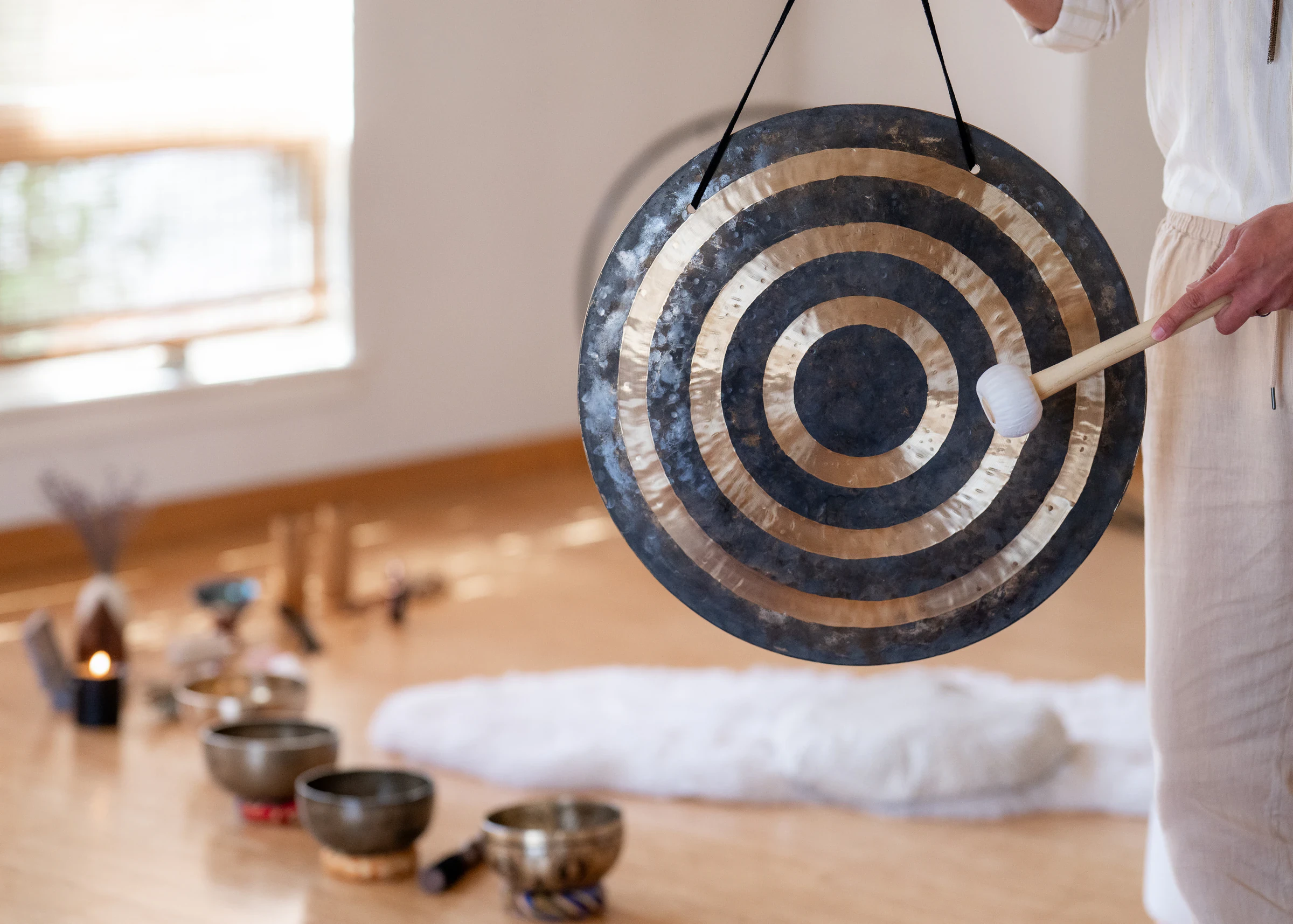 Matias playing a hanging gong with a mallet, singing bowls on the floor behind