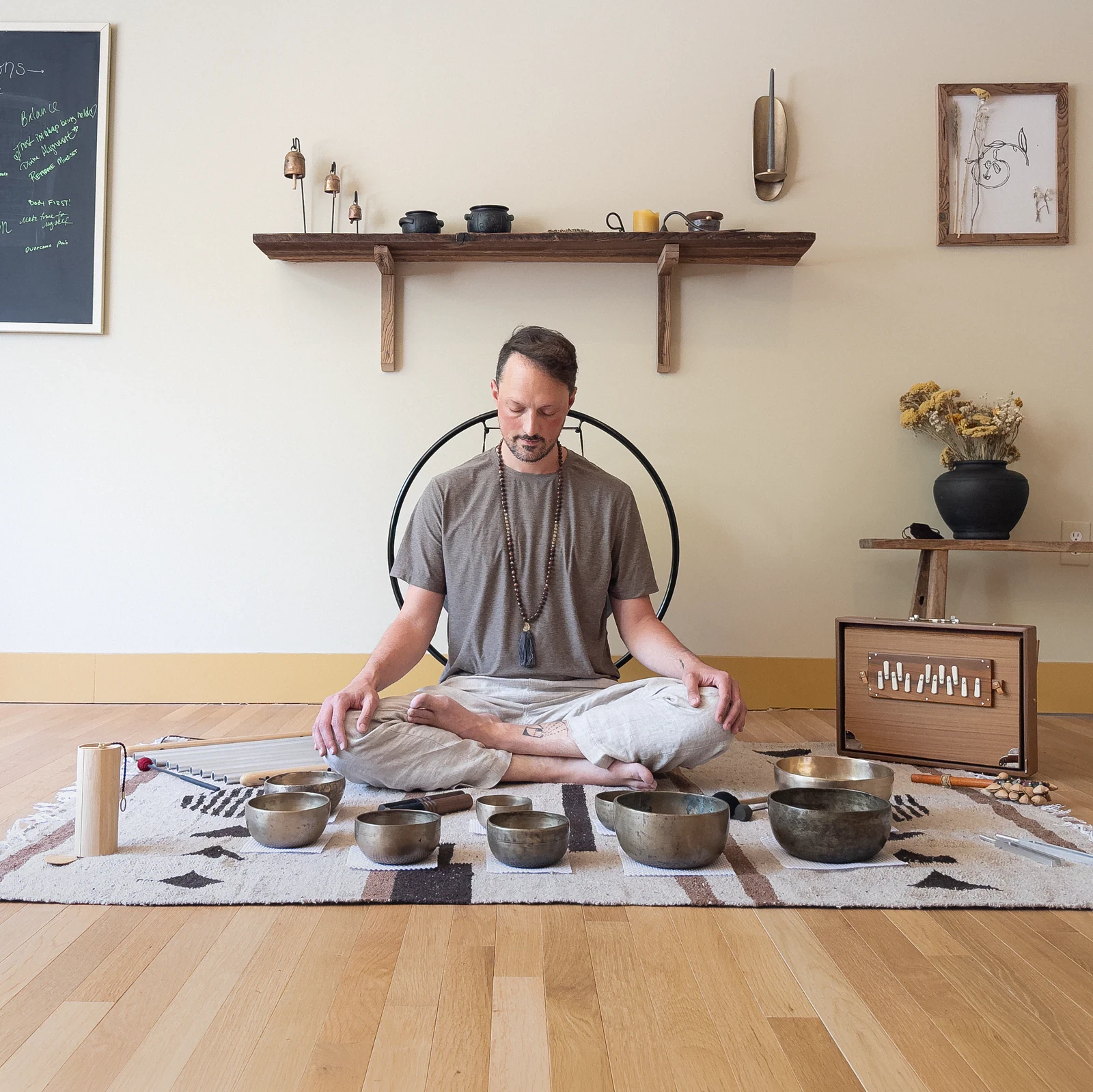 Matias meditating cross-legged on a rug, hands on his knees, Tibetan singing bowls and a shruti box around him